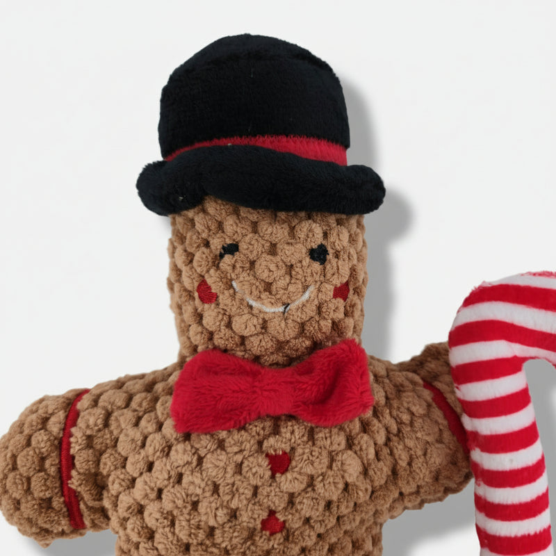 Gingerbread-shaped Christmas plush dog toy with soft textured fabric, red bow, and built-in squeaker.